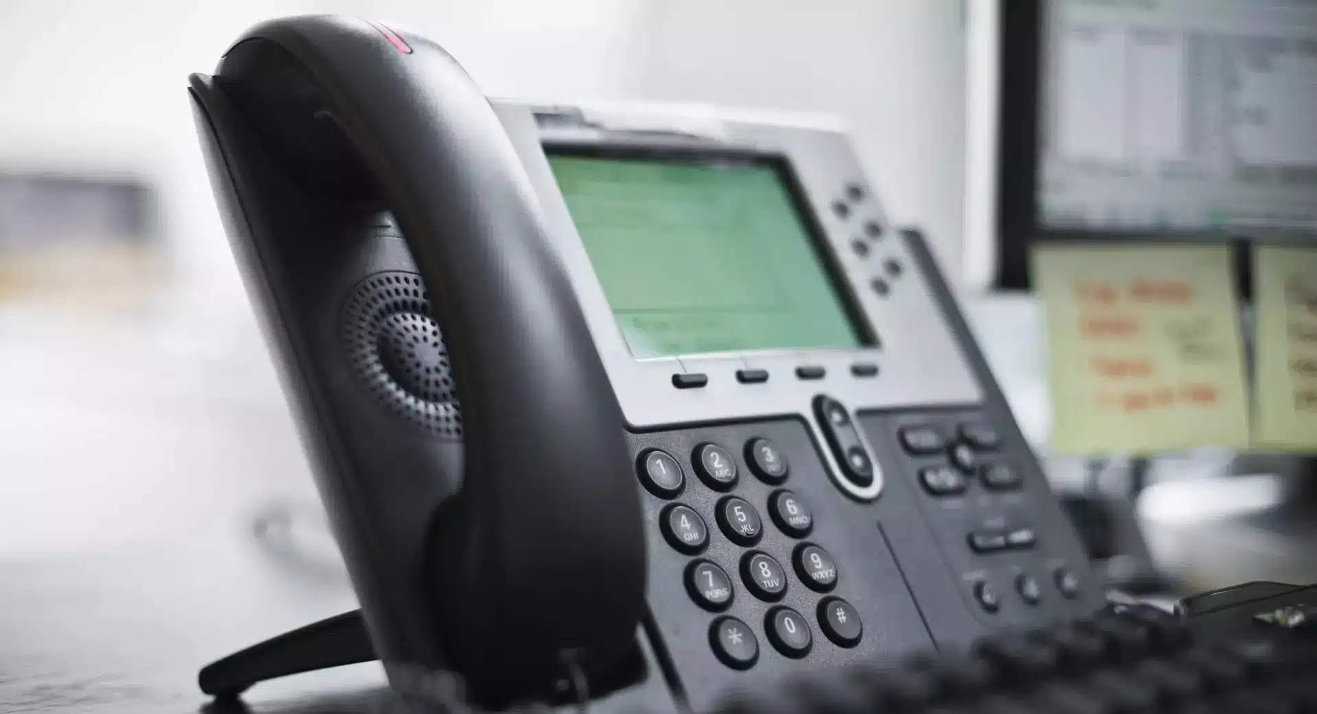 Close-up of an office telephone switchboard with a digital screen, keypad, and handset, symbolizing the transition from a traditional switchboard to a virtual receptionist system.