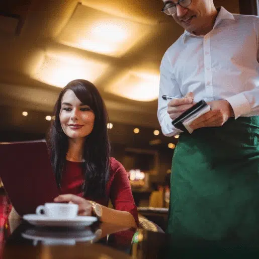 Smiling woman placing an order with a waiter in a restaurant, representing the importance of a restaurant answering service for customer support.
