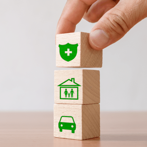 Hand stacking wooden blocks with icons for auto, home, and health—representing comprehensive insurance answering service solutions.