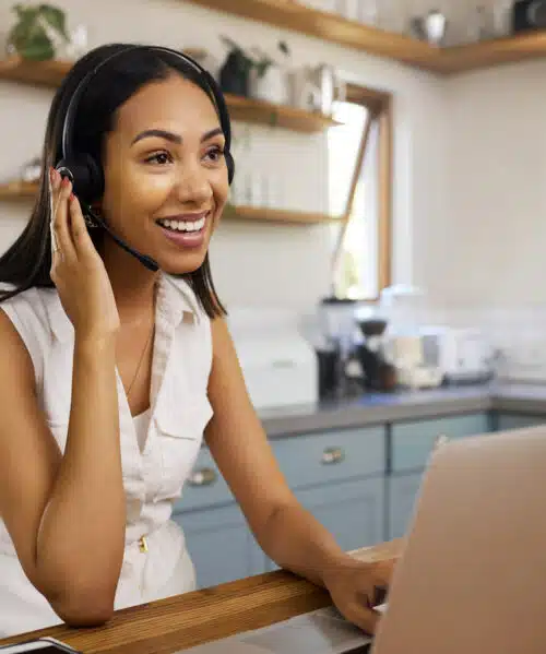 Smiling virtual receptionist using a headset and laptop in a home office setting, representing customized call handling for professional business support.