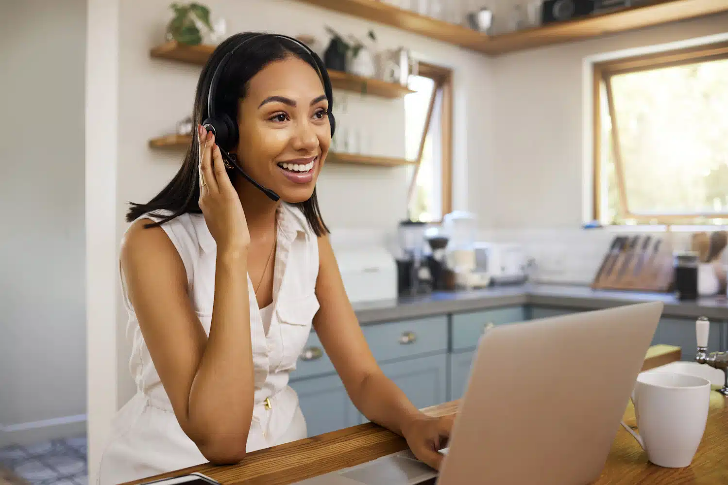 Smiling virtual receptionist using a headset and laptop in a home office setting, representing customized call handling for professional business support.