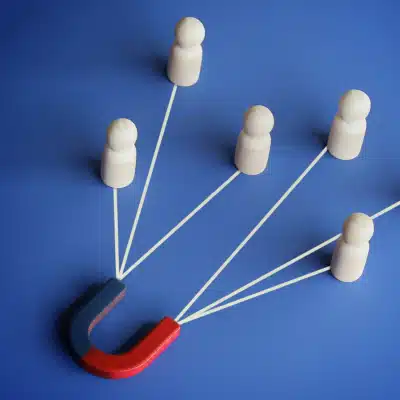 A red and blue magnet attracting five wooden figurines with white lines, symbolizing customer retention or lead generation on a blue background.