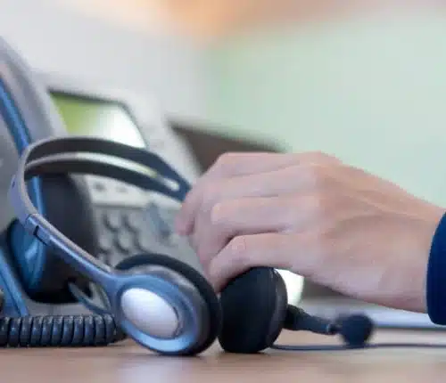 Close-up of a person holding a headset near a phone switchboard.