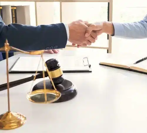 A lawyer and client shaking hands with a gavel and scales of justice on the table.