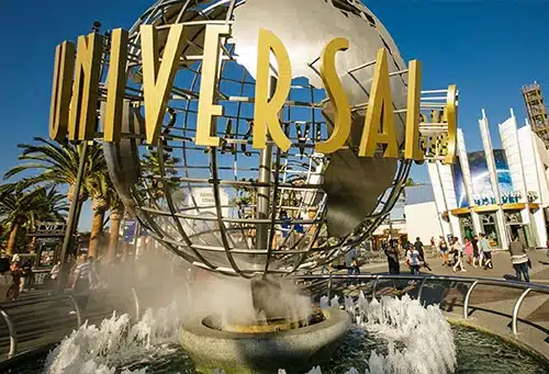 Universal Studios globe entrance in Los Angeles with visitors and water fountains.