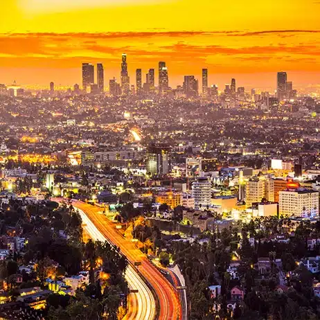 Los Angeles city skyline at sunset with highway lights and buildings in the distance.