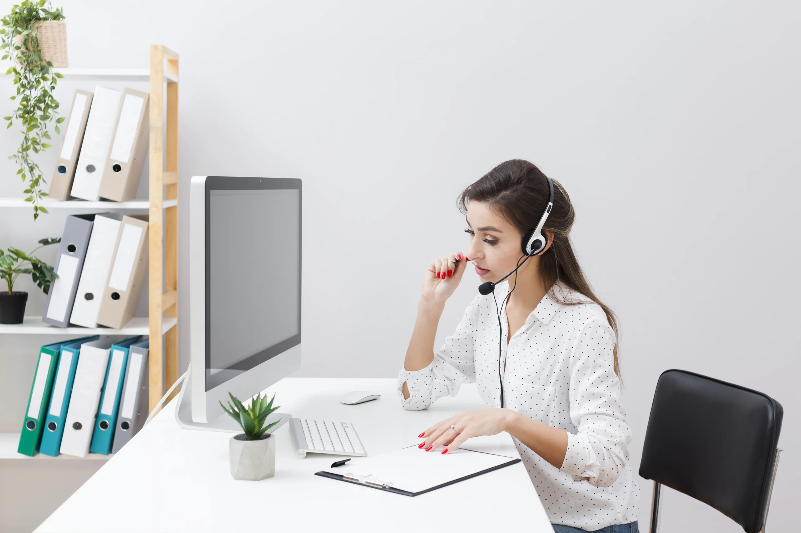 A virtual receptionist sitting at a desk with a computer, writing notes, and focused on her work.