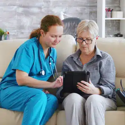 Home care nurse assisting elderly woman with tablet, providing support and personalized care at home.