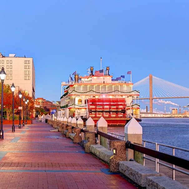 Riverboat docked along the Savannah, Georgia waterfront at dusk with a cable-stayed bridge in the background.