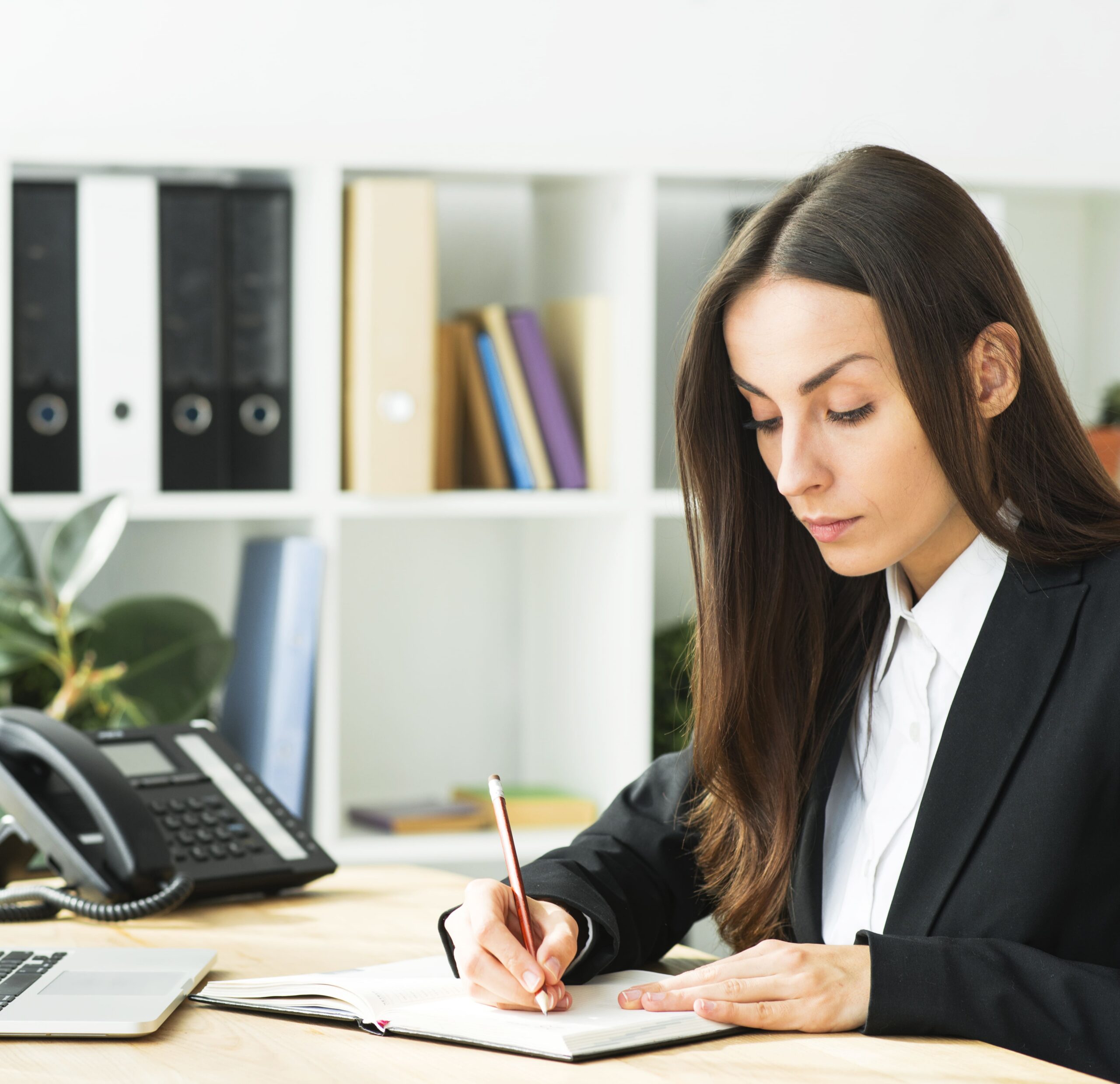 Professional Tax consultant writing notes at office desk with laptop, files, and phone in modern workspace