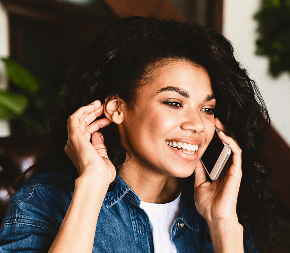 Woman with curly hair smiling while talking on her phone
