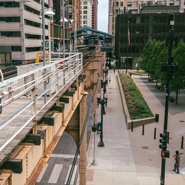 Elevated train tracks beside a downtown Chicago street and tree-lined green space